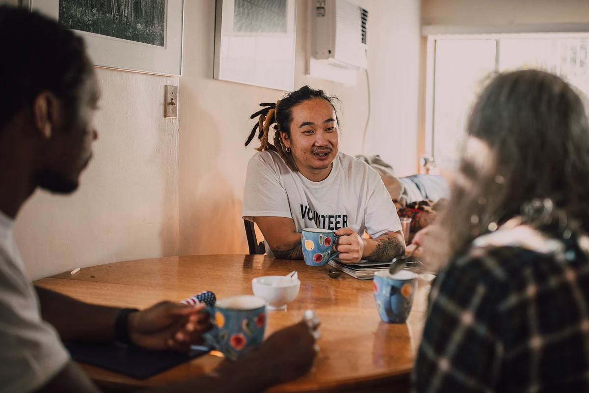 3 students sit at a table drinking out of mugs