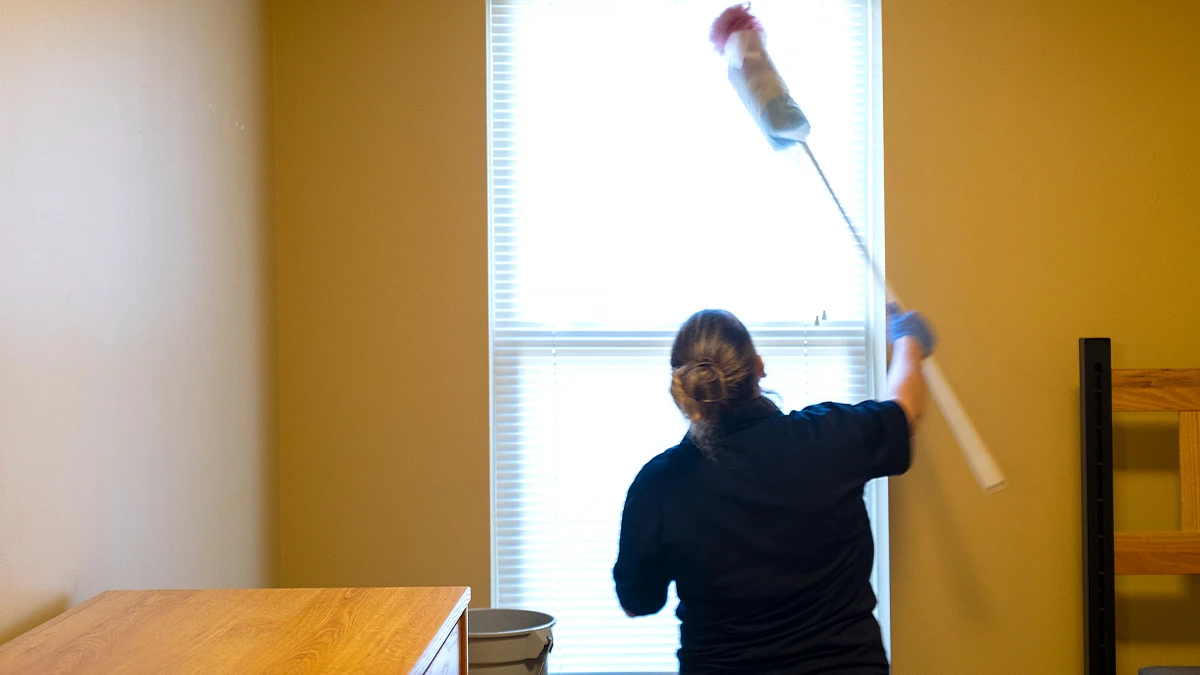 UNC Housekeeping staff member Jennifer King dusts window blinds in a recently vacated residence hall room. (Jon Gardiner/UNC-Chapel Hill)