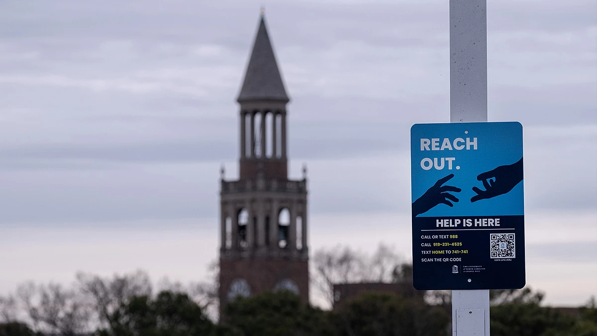 A sign offering mental health support information is placed in front of a tall, pointed tower under a cloudy sky.