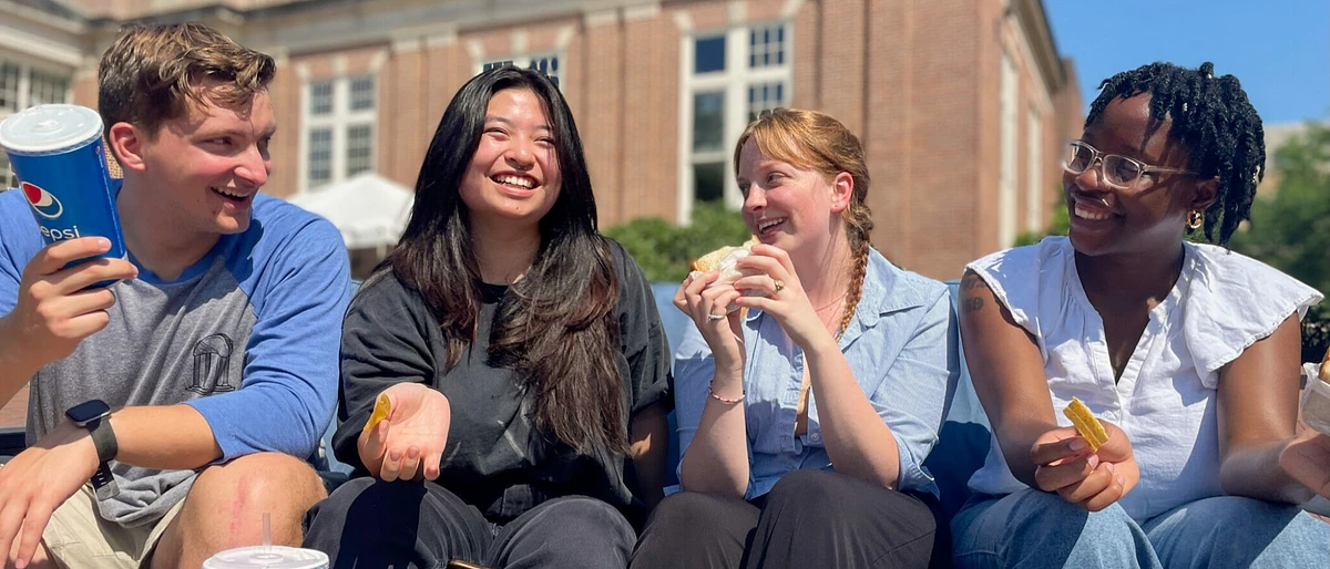 Four people are sitting together outdoors, smiling and enjoying snacks.